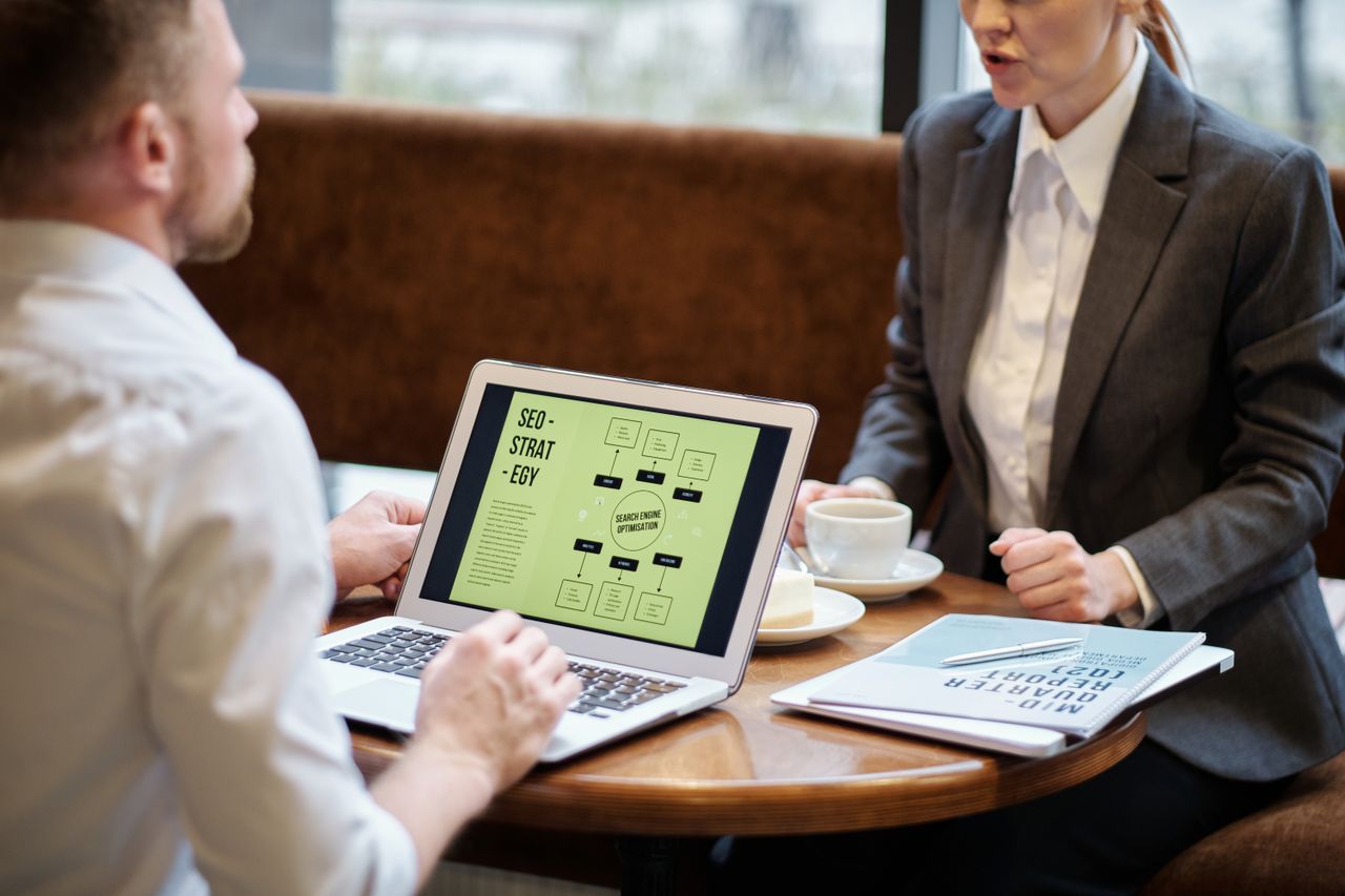 Un homme et une femme participent à une réunion professionnelle dans un café chaleureux pour discuter de stratégie SEO.