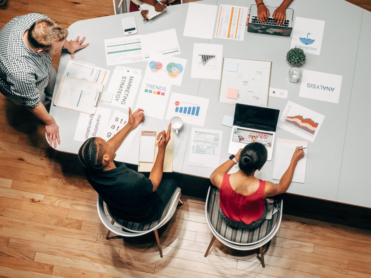 Overhead view of a diverse team of coworkers in a business meeting, discussing strategies with charts and laptops.